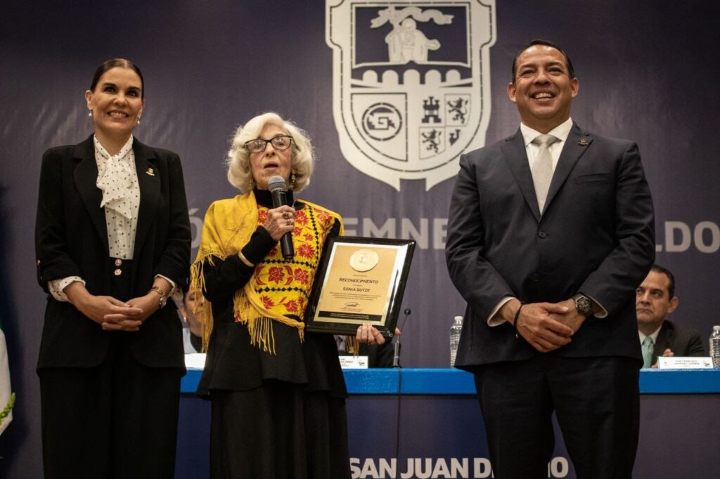 Cancelan sello postal conmemorativo de la fundación de San Juan del Río y reconocen a sanjuanenses distinguidos • Genoveva Sonia Butze Aguilar, impulsora del Museo Panteón de la Santa Vera Cruz, y el padre misionero xaveriano, Pablo Zurlo Zordonatzzo, recibieron la distinción. • El presidente municipal, Roberto Cabrera Valencia, se trasladó al Jardín Fundadores, donde montó una guardia de honor, acompañado de integrantes del Ayuntamiento y del Gabinete Municipal. San Juan del Río cumple 494 años y lo hace de pie, con dignidad y con rumbo, sostuvo el presidente municipal sanjuanense, Roberto Cabrera Valencia, en su mensaje con motivo de la sesión solemne de Cabildo, en la que se llevó a cabo la cancelación especial del sello postal conmemorativo de la fundación de la ciudad y la entrega de reconocimientos a sanjuanenses distinguidos. Durante la sesión, realizada en el Foro San Juan del Portal del Diezmo, Roberto Cabrera agradeció a quienes aman y cuidan a San Juan del Río; a quienes sueñan en grande y trabajan con humildad; a quienes saben que la historia se honra con palabras y obras. Recordó que San Juan del Río se prepara para cumplir medio siglo, con la frente en alto y con el corazón dispuesto, pues, enfatizó, la mejor manera de honrar el pasado es cumplirle al presente y sembrar progreso en el futuro. “Hoy, como cada 24 de junio, nos reúne la memoria de un pueblo que nació a orillas de un río generoso, que con su cauce marcó el destino de generaciones enteras. San Juan del Río cumple hoy 494 años de fundación, y lo celebramos con orgullo, con gratitud y con profunda responsabilidad. Esta sesión solemne de Cabildo tiene un significado especial. Porque no sólo estamos conmemorando una fecha: Estamos reconociendo un legado. Un legado que nos compromete. Un legado que tiene nombre y sentido: el Legado de Bien Común”, dijo Cabrera Valencia. Tras la lectura de la reseña histórica de la fundación de San Juan del Río, a cargo de la síndica del Ayuntamiento, Rosalba Ruiz Ramos, el presidente municipal sanjuanense, Roberto Cabrera Valencia, acompañado de la Reina de la Feria Nacional Ganadera San Juan del Río 2025, Hanney I, y el gerente estatal de Correos de México en Querétaro, Juan Manuel Contreras Espinoza, realizaron la cancelación especial del sello postal. Posteriormente, el alcalde de San Juan del Río entregó un reconocimiento como sanjuanense distinguida a Genoveva Sonia Butze Aguilar, investigadora del Instituto Nacional de Antropología e Historia (INAH) e impulsora del Museo Panteón de la Santa Vera Cruz (antes Museo de la Muerte), además de conservadora del patrimonio, tradiciones y educación, entre otras actividades relacionadas con la actividad museográfica. El padre misionero xaveriano, Pablo Zurlo Zordonatzzo, de manera póstuma, también fue distinguido con el reconocimiento de sanjuanense distinguido. En representación del galardonado, el misionero xaveriano y superior del Seminario de San Juan del Río, Samuel Godínez Uribe, recibió la distinción de Pablo Zurlo, quien se caracterizó por el desarrollo de las personas de este municipio. En la sesión solemne de Cabildo estuvieron presentes las y los integrantes del Ayuntamiento de San Juan del Río, miembros del Gabinete Municipal, familiares de los y las galardonadas, entre otras personalidades, quienes, en conjunto con el presidente municipal, Roberto Cabrera Valencia, se trasladaron al Jardín Fundadores, donde montaron una guardia de honor, y a la Parroquia de San Juan Bautista.